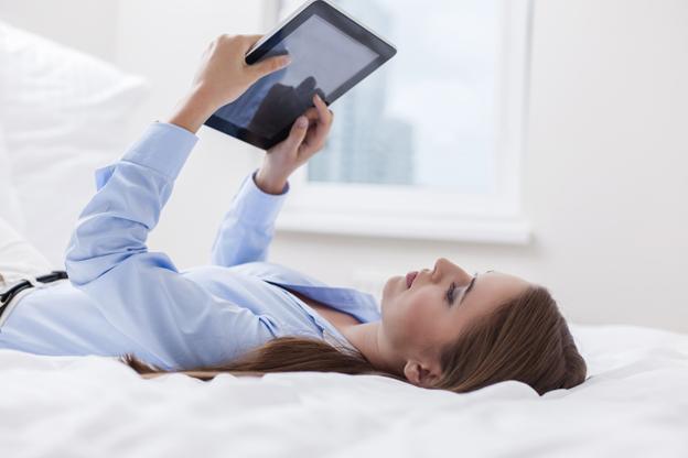 Woman lying on bed watching something on tablet