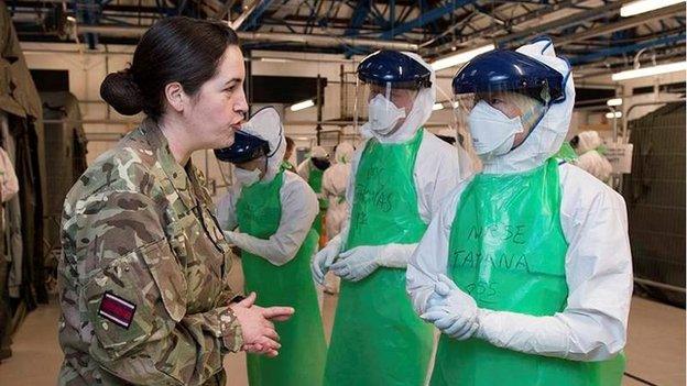 A soldier in camouflage uniform talking to people dressed in protective medical gear