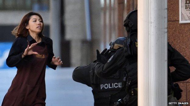 A former hostage wearing a Lindt uniform runs towards police from a cafe in central Sydney where a gunman is holding people captive