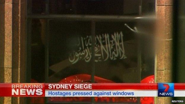 Black flag bearing the shahada held up to a window of the Lindt Cafe in Sydney, Australia, on 15 December 2014