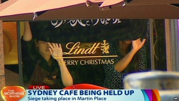 This image taken from video shows people holding up what appeared to be a black flag with white Arabic writing on it, inside a cafe in Sydney, Australia Monday, Dec. 15, 2014