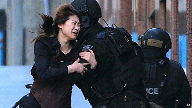 A hostage runs to armed tactical response police officers for safety after she escaped from a cafe under siege at Martin Place in the central business district of Sydney, Australia, Monday, Dec. 15, 2014.