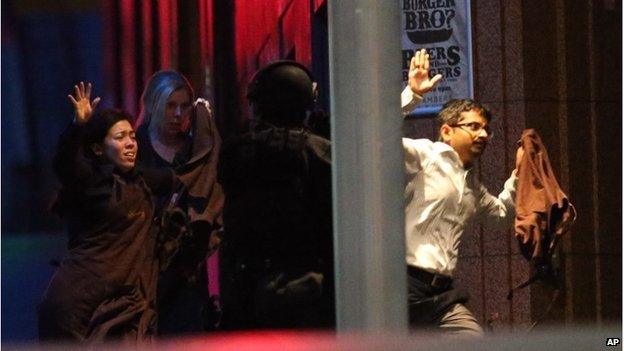 Hostages run towards armed tactical response police as they run to freedom from a cafe under siege at Martin Place in the central business district of Sydney, Australia, Tuesday, Dec. 16, 2014.