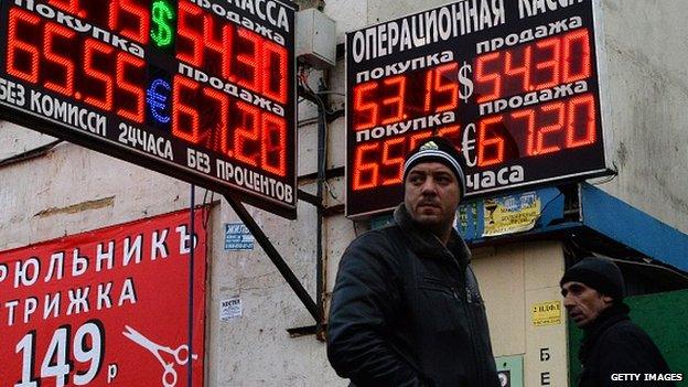 Pedestrians walk past a board listing foreign currency rates against the Russian rouble outside an exchange office in Moscow on December 3, 2014