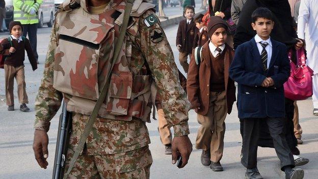 A Pakistani soldier stands guard as parents leave with their children near the site of an attack by Taliban gunmen on a school in Peshawar on 16 December 2014