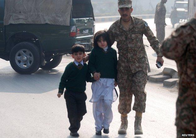 A soldier escorts schoolchildren away from the Army Public School in Peshawar, 16 December 2014