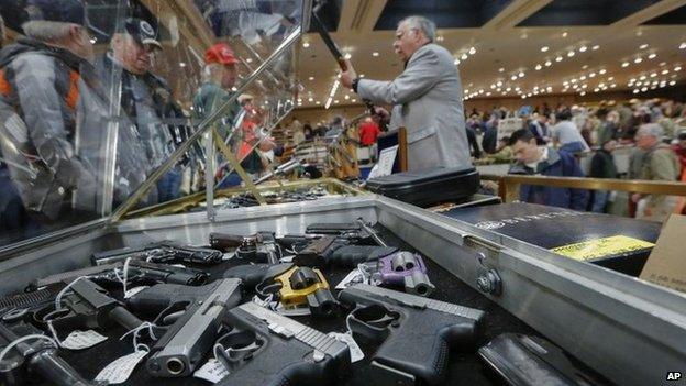 In this 26 January, 2013 file photo, handguns appear on display at the table of David Petronis of Mechanicville, NY, standing with rifle.