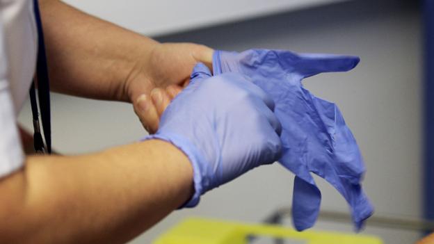 NHS worker puts on surgical gloves