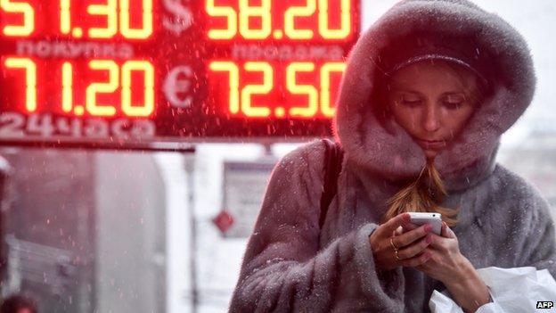 A woman walks past a board listing foreign currency rates against the Russian rouble outside in central Moscow on December 12, 2014.