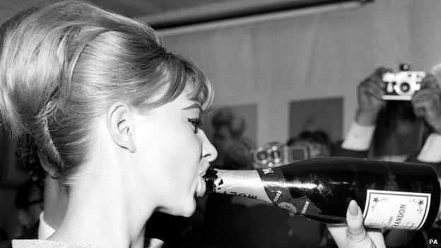 Mandy Rice-Davies drinking a bottle of champagne in July 1963