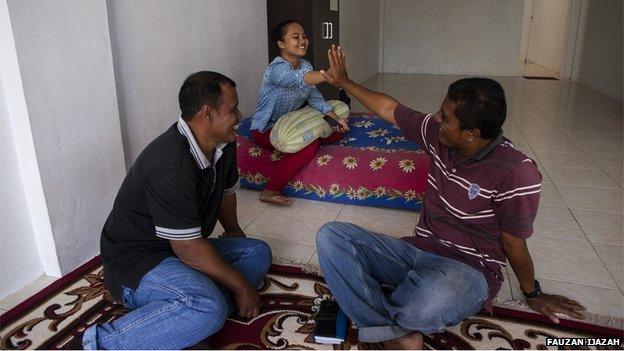 Rina and her father Mustafa sit in a room with Save the Children volunteer Idil Saputra