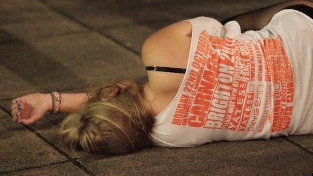 Young woman lies on the pavement in Brighton, having drunk too much