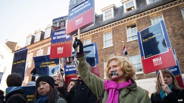 A demonstrator wearing tape on her mouth holds up a pair of handcuffs and a placard as she joins a protest outside the Egyptian embassy in central London on December 29, 2014
