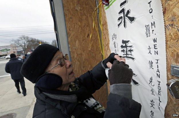 A man puts up a commemorative banner at the wake of New York Police Officer Wenjian Liu, 3 January