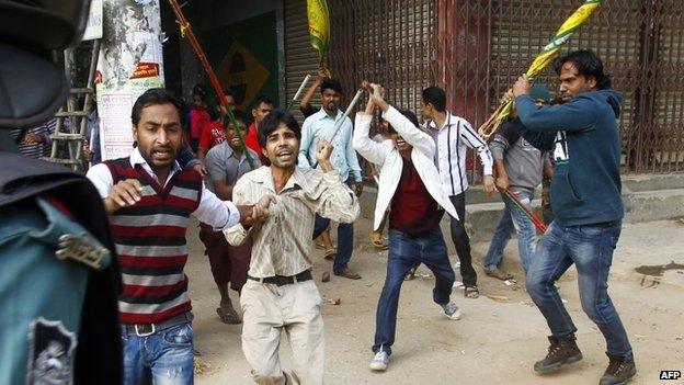 A Bangladeshi policeman (left) looks on as government party activists (right) wield sticks against activists of the Bangladesh National Party (BNP) during a clash in Dhaka (05 January 2015)