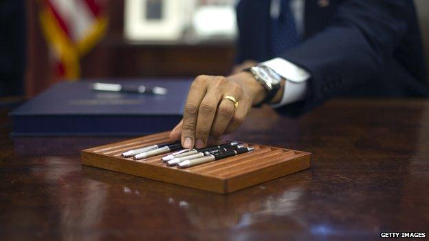 S President Barack Obama reaches for a pen to sign bills the Oval Office of the White House in Washington, DC, November 27, 2013