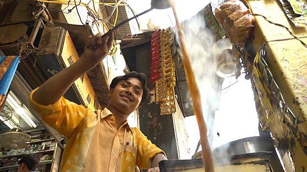 A chai wallah doing acrobatics with a steaming infusion