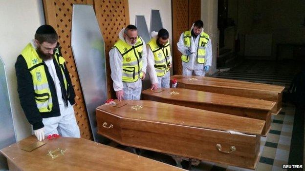 Members of the Zaka emergency response team pray beside the coffins of four victims of an attack at a kosher supermarket on Friday, before their transport from Paris to Israel for burial, 12 January 2015