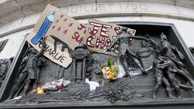 Placard with a news cartoon by French cartoonist Plantu is seen placed amongst other tributes on the statues at the Place de la Republique in Paris