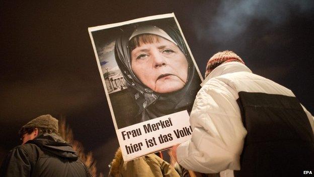 A participant in a rally with the Anti-Islamic Pegida (Patriotic Europeans against the Islamization of the West) movement holds up a picture of Chancellor Merkel wearing a headscarf written with the words "Mrs. Merkel - here is the people" in Dresden, Germany, 12 January 2015