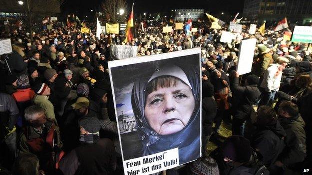 A protestor holds a poster showing German Chancellor Angela Merkel wearing a head scarf in front of the Reichtstags building with a crescent on top and the writing "Mrs Merkel here is the people" during a rally of the group Patriotic Europeans against the Islamization of the West, or PEGIDA, in Dresden, Germany, Monday, Jan. 12, 2015.