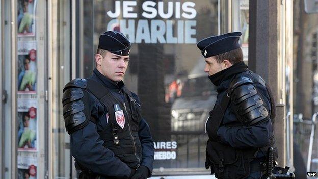 French police stand close to a sign that reads 'Je Suis Charlie' (I am Charlie), referring to Charlie Hebdo, the satirical magazine whose Paris offices were attacked by brothers, French nationals Cherif and Said Kouachi last week, on January 11, 2015