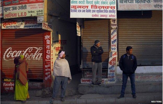 Nepalese stand in front of a closed shops as they look towards protesters (unseen) during the general strike in Kathmandu 13 January 2015.