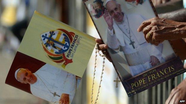 Sri Lankan Christians hold paraphernalia bearing the portrait of Pope Francis as they wait for his arrival in Colombo