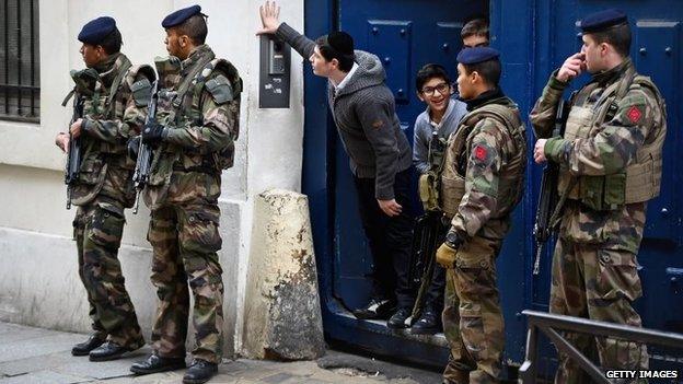 Children look out from a doorway as armed soldiers patrol outside a school in the Jewish quarter of the Marais district in Paris, France, 13 January 2015