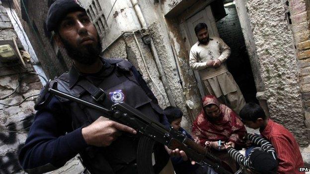 A member of the Pakistani security services stands guard while a health worker administers a polio vaccine to a child, in Peshawar, Pakistan, 20 December 2014