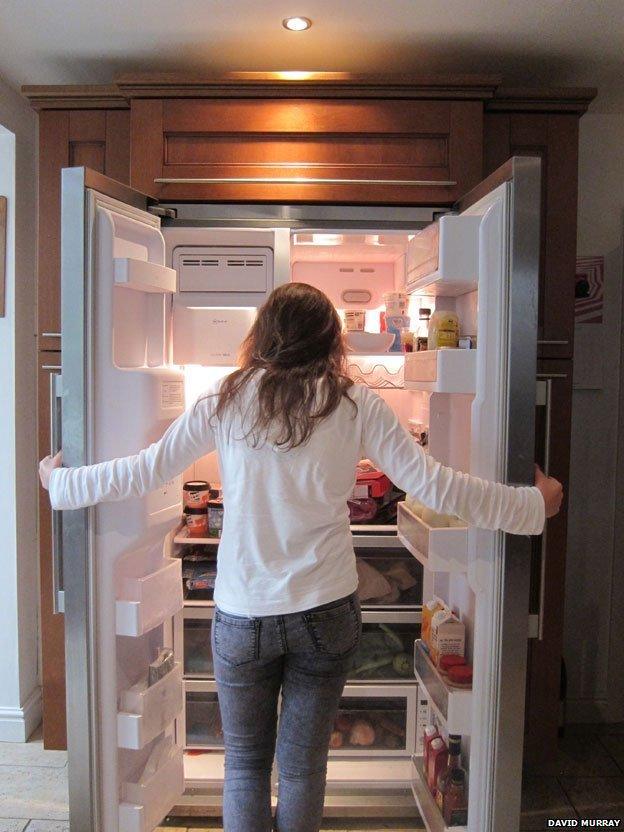 A woman in front of a well stocked fridge