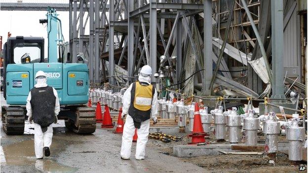 Workers wearing protective gears stand outside the Unit 4 reactor at the Fukushima Dai-ichi nuclear power plant in Okuma, Fukushima prefecture, northeastern Japan, Wednesday, 12 November 2014