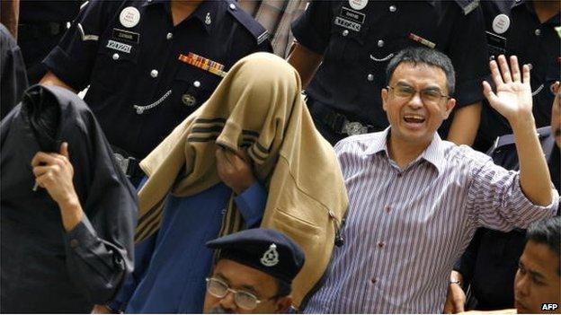 Charged political analyst Abdul Razak Baginda (R) waves to photographers as he and charged special unit police officers Sirul Azhar Umar (C) and Azilah Hadri (L) cover their faces while being escorted out of court during an intermission in Shah Alam, near Kuala Lumpur, 29 June 2007