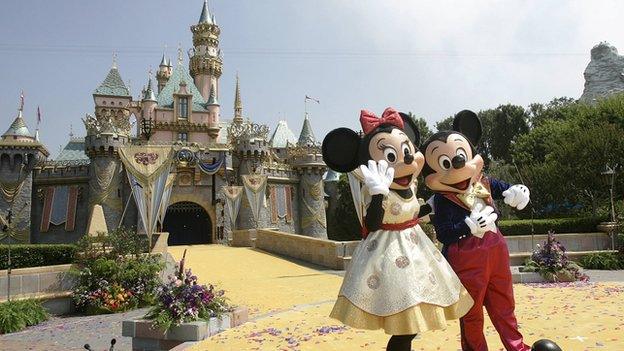 Mickey and Minnie Mouse stand outside Cinderella's castle at Disneyland.