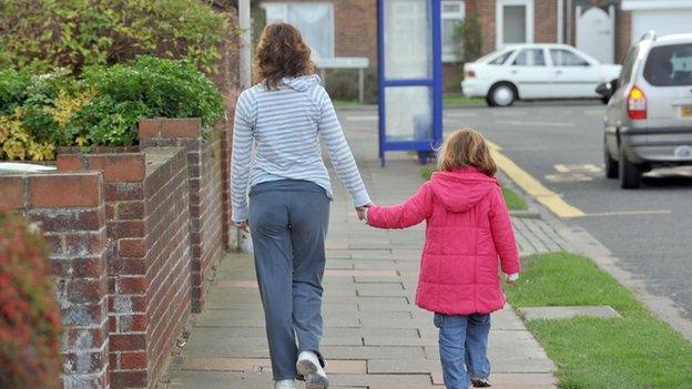 mother walking down street hand-in-hand with daughter