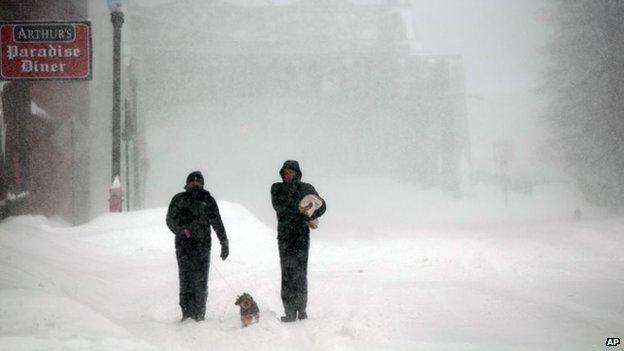 Two pedestrians and a dog brave the storm in the US