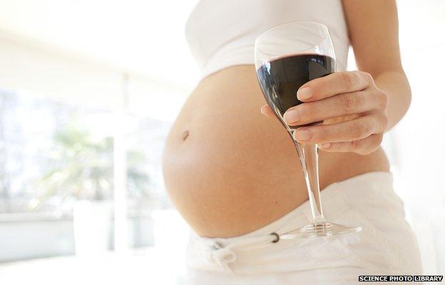 Pregnant woman's stomach and her holding a glass of wine