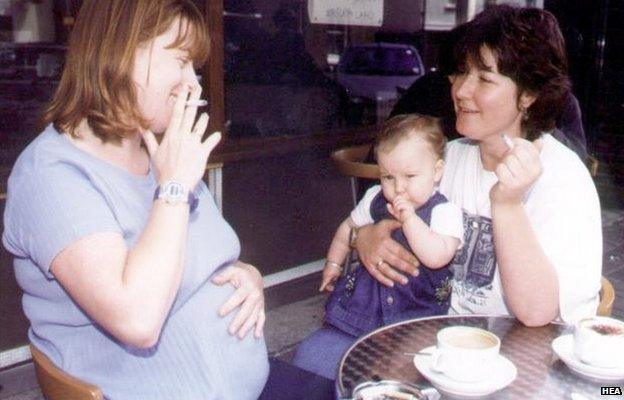 Pregnant woman and woman with baby on her lap, both smoking