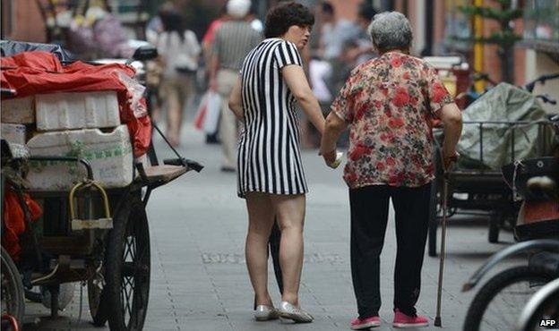 A daughter helps her elderly mother walking along a street in China