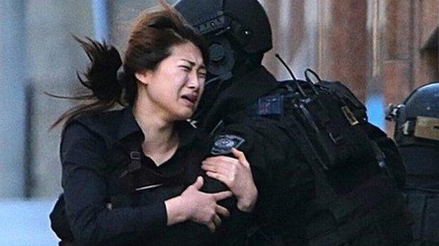 A hostage runs to armed tactical response police officers for safety after she escaped from a cafe under siege at Martin Place in the central business district of Sydney, Australia, Monday, Dec. 15, 2014.