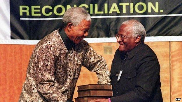 Then-South African President Nelson Mandela (L) receives a five volumes of Truth and Reconciliation Commission final report from Archbishop Desmond Tutu, in Pretoria 29 October 1998