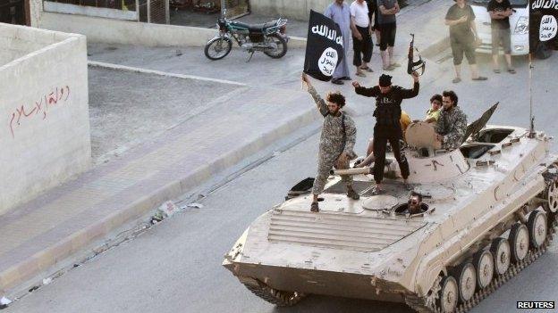 Militant Islamist fighters hold the flag of Islamic State (IS) while taking part in a military parade along the streets of northern Raqqa province