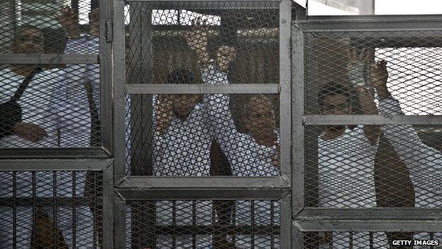 Australian journalist Peter Greste of al-Jazeera and his colleagues stand inside the defendants cage during their trial for allegedly supporting the Muslim Brotherhood