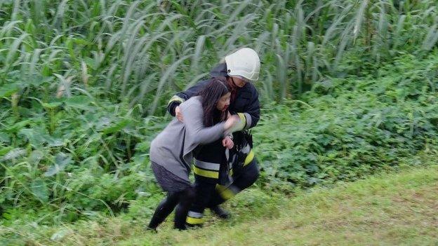 An injured passenger is escorted up the river bank by one of the rescue workers