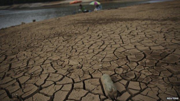 A bottle is seen on cracked ground as men fish at the Atibainha dam, as the lake dries up due to a prolonged drought in Nazare Paulista, Sao Paulo state, in this October 17, 2014