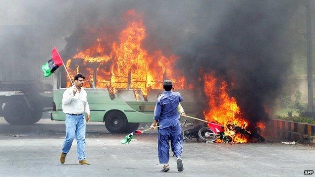 Pakistani opposition parties activists walk alongside burning vehicles after clashes erupted between the government and opposition parties supporters in Karachi, 12 May 2007