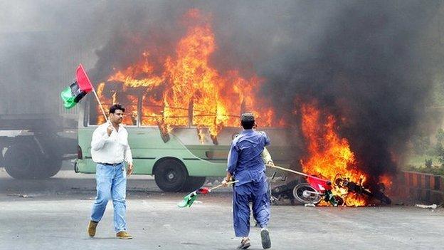 Pakistani opposition parties activists walk alongside burning vechiles after clashes erupted between the government and opposition parties supporters in Karachi, 12 May 2007