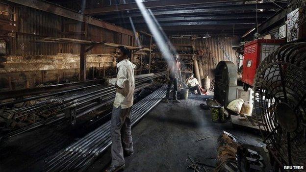 A worker carries an iron pipe inside a metal fabrication workshop in an industrial area of Mumbai February 9, 2015