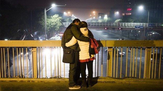 In this picture taken on November 20, 2014 a couple kiss on a pedestrian bridge as thick smog covered Beijing.