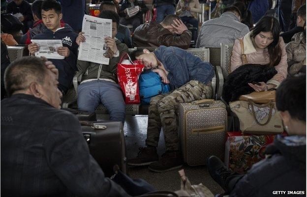 A Chinese traveller sleeps as others read and relax as they wait to leave for the Spring Festival at a local railway station on 17 February 2015 in Beijing, China.